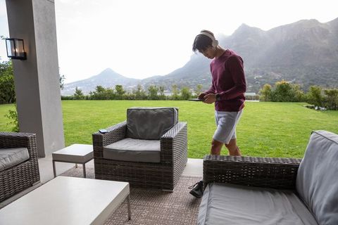 Young man wearing headphones walking on patio with mountain view and wicker furniture