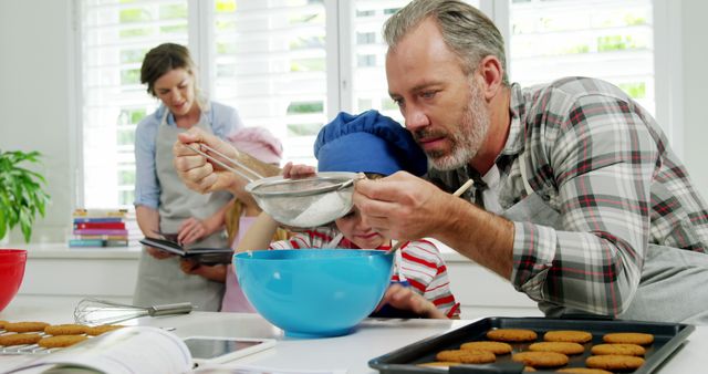 Father and son are sifting flour into blue bowl while mother reads recipe with daughter. This image is ideal for content related to family bonding, home baking, cooking projects, and illustrating daily domestic activities. It can be used in articles, advertisements, blogs, and promotional materials that focus on family togetherness, cooking tips, or parenting.