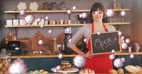 Confident bakery worker holding open sign amidst virus illustrations