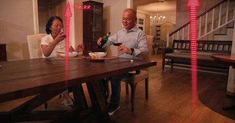 Mature couple pouring wine at cozy wooden dining table during warm evening