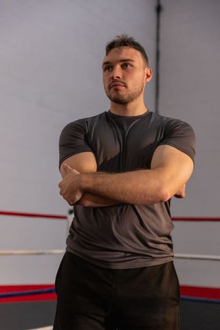 Focused male boxer standing with arms crossed in boxing ring wearing fitted gray shirt