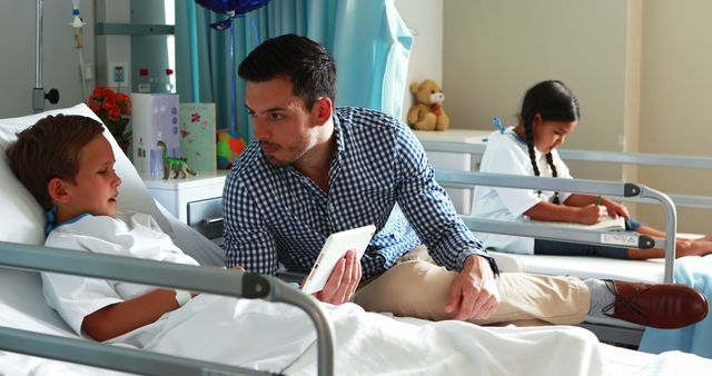 Father Visiting Son in Hospital Showing Him Tablet with Daughter in Background - Download Free Stock Images Pikwizard.com