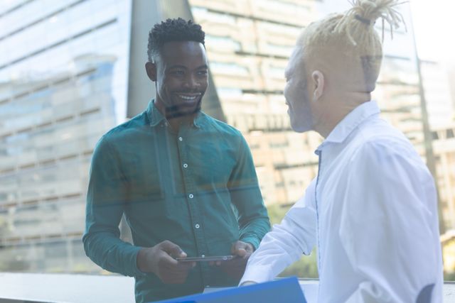 Smiling african american mid adult businessman with albino male colleague standing in office balcony. unaltered, abnormal, technology, data, corporate business, occupation and office concept.