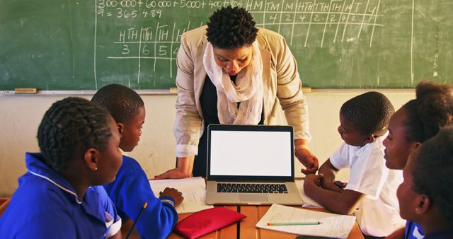 Teacher engaging a group of African students in an interactive lesson using a laptop in the classroom. Suitable for topics on modern education methods, digital learning, group activities in school, teaching practices, and educational technology.