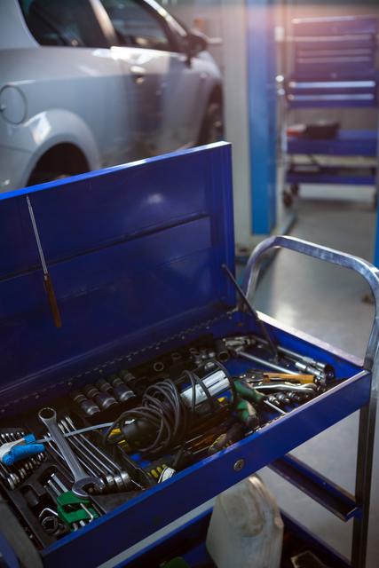 This image shows a close-up of a blue toolbox filled with various tools in a repair garage. Ideal for use in articles or advertisements related to automotive repair, mechanical services, or industrial maintenance. It can also be used in blogs or websites that focus on DIY car repairs, professional mechanics, or engineering workshops.