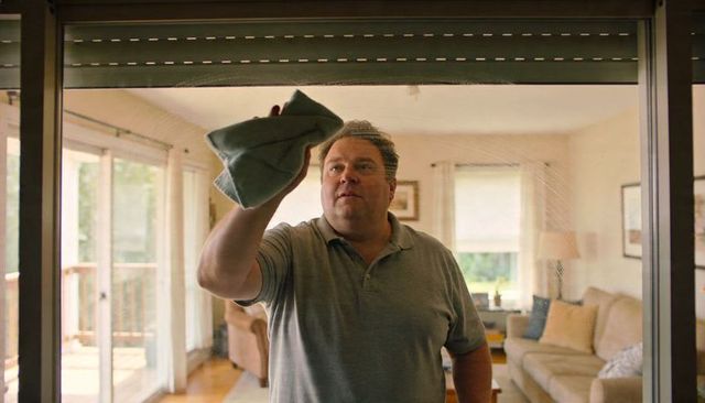 Middle-aged man wiping sliding glass door in cozy living room, homeowner cleaning routine