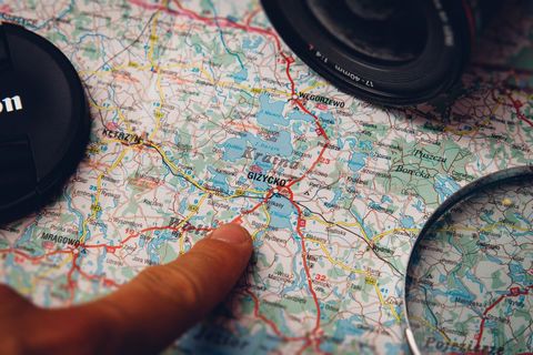 Finger pointing at map near camera lens planning road trip around masurian lakes poland