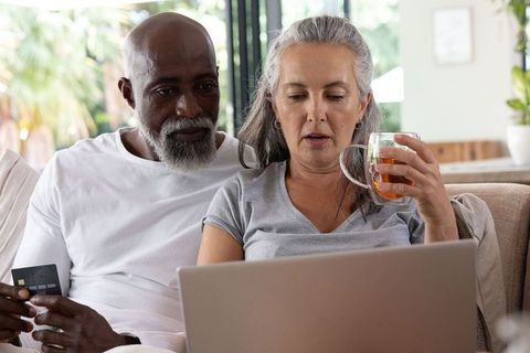 Mature couple using laptop on sofa making online purchase and managing household finances