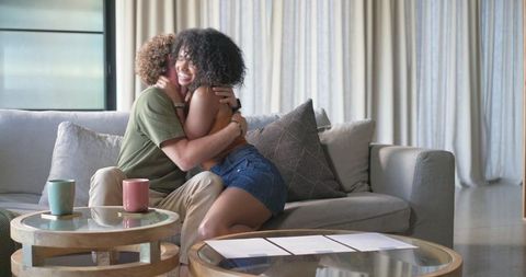 Couple hugging on sunlit modern sofa, sharing joy and cozy weekend moment at home