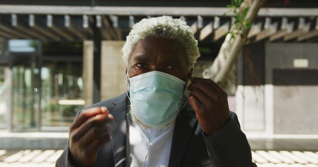 Portrait of african american senior man in facemask wearing earphones in corporate park. hygiene and social distancing during coronavirus covid-19 pandemic.