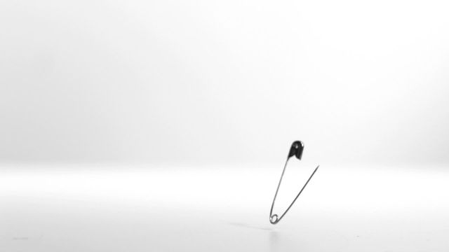 Open safety pin vibrating mid-air against a white background, creates a minimalist and simple effect highlighting the delicate balance and tension. Ideal for use in educational videos demonstrating physics, advertisements for office supplies, and artistic projects emphasizing minimalistic design or tension concepts.