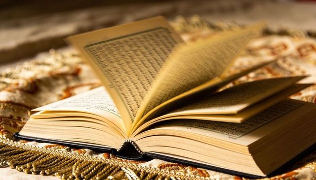 Open arabic manuscript on ornate woven rug with fanned pages, sewn spine, tassel fringe