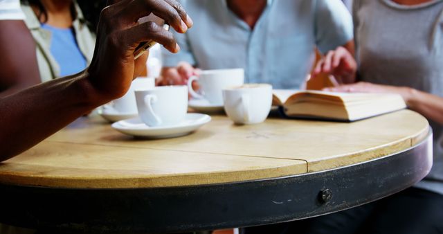 Diverse group of friends socializing around a table at a coffee shop. Great for illustrating themes of casual meetings, friendship, diversity, leisure, and urban lifestyle in blog articles, social media posts, or advertisements.