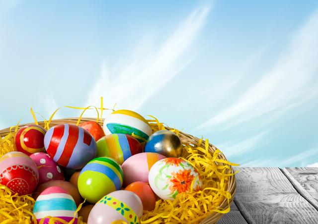 Brightly decorated Easter eggs layered in straw within a basket, against a bright blue sky backdrop, symbolizes renewal and spring. Ideal for Easter promotions, holiday greetings, and festive event invitations.