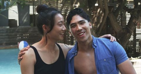 Diverse couple laughing poolside at backyard summer gathering, relaxed vibrant moment