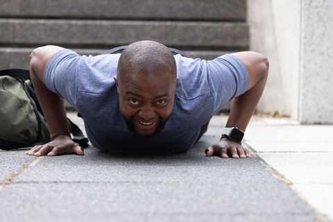 Smiling man performing push-ups on city steps wearing smartwatch and backpack