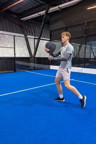 Young athlete preparing forehand on blue padel court, energetic wide stance and focus