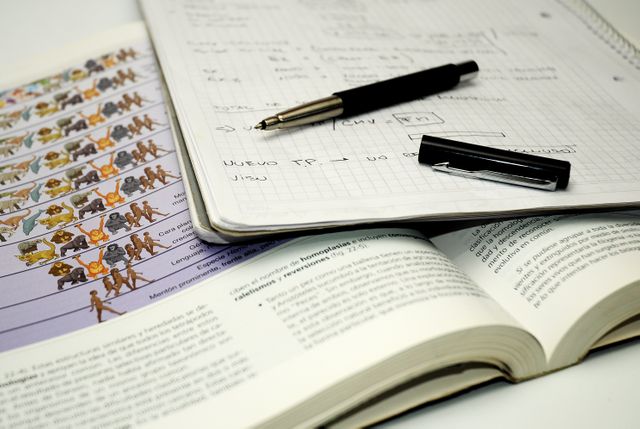This close-up image shows biochemistry study materials, including open textbooks, a notebook with handwritten notes, and a pen, focusing on evolutionary diagrams and equations. Ideal for educational content, study-related themes, and academic illustrations.