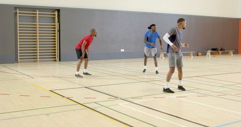 Three players defending on indoor basketball court showing teamwork, movement and focus