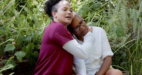 Son embracing senior mother on garden bench showing affection