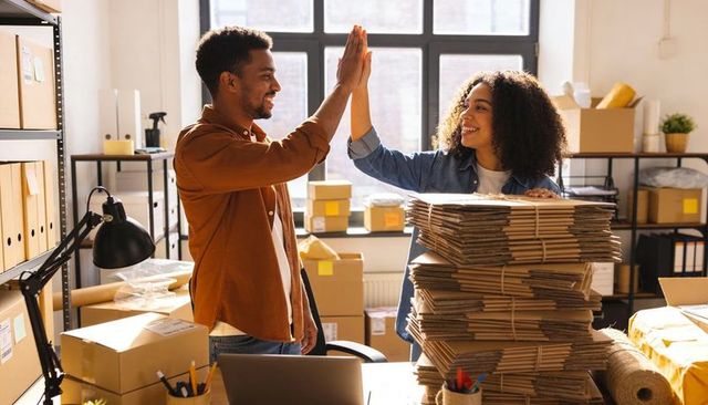 Small business team high-fiving while packing orders in bright fulfillment workspace