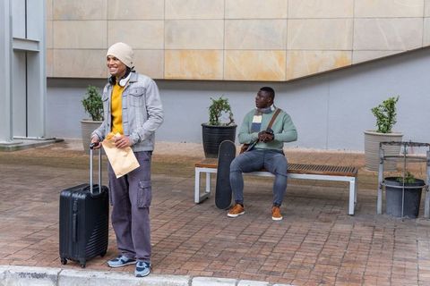 Diverse young men traveling and hanging out in urban plaza with suitcase and skateboard