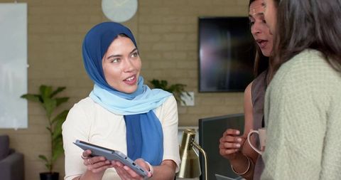 Diverse female team collaborating over tablet in modern office with whiteboard