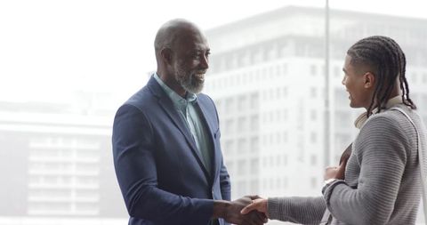 African American Executive Shaking Hands with Young Professional in Modern Office Lobby