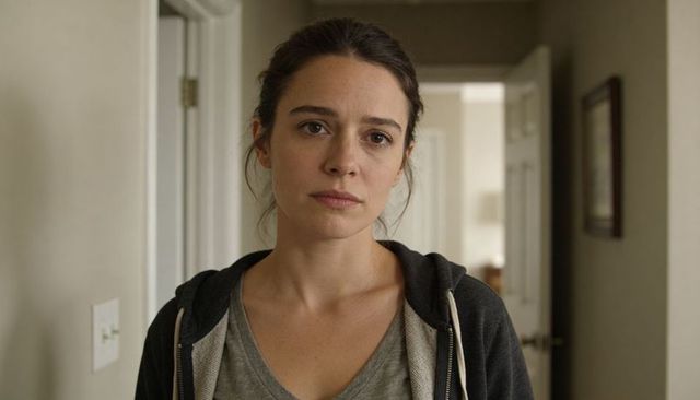 Pensive young woman standing in hallway wearing grey t-shirt and hoodie, portrait