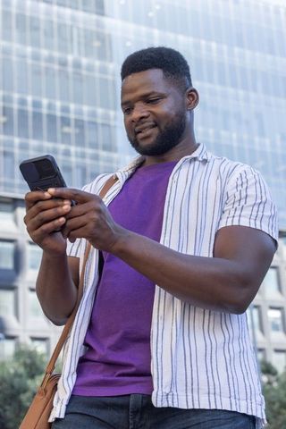 African american man checking smartphone in city plaza outside glass office tower