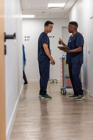 Diverse healthcare team reviewing clinical data in radiology corridor with tablet and med cart
