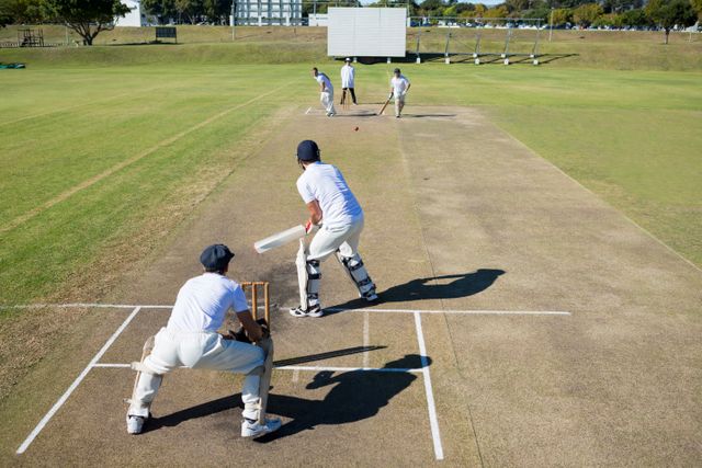 High angle view of a cricket match in progress on a sunny day. Players are actively engaged in the game on a well-maintained field. Ideal for use in sports-related articles, advertisements for cricket equipment, or promotional material for outdoor activities and team sports.