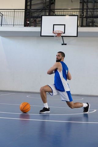 Male Basketball Player Lunging on Indoor Court with Ball