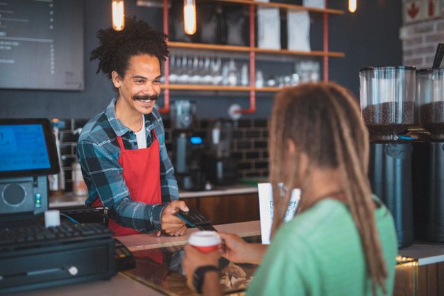 Happy biracial male barista with moustache taking payment for coffee in cafe. independent small business in a city.