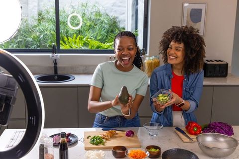 Diverse friends cohosting cooking show, prepping avocado cucumber bowl in modern kitchen
