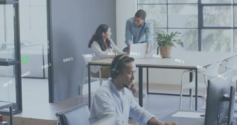 Support agent wearing headset typing at workstation in bright open-plan office with colleagues