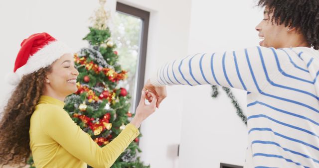 Couple joyfully dancing by a decorated Christmas tree at home. Ideal for holiday season promotions, festive greetings cards, social media posts about Christmas celebrations or content highlighting couples enjoying holiday traditions together.