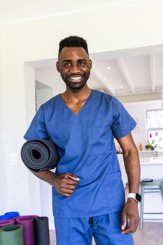 Smiling healthcare professional in blue scrubs holding yoga mat for wellness and fitness
