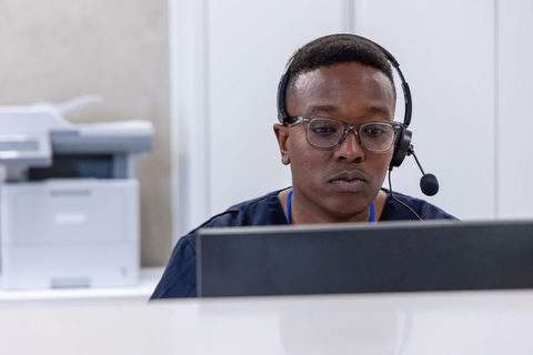 Focused african receptionist wearing headset and glasses working at front desk computer