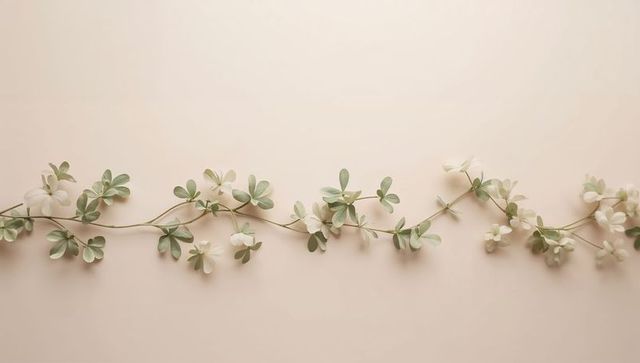 Minimalist Pale Vine Garland with White Flowers Lying on Soft Beige Background