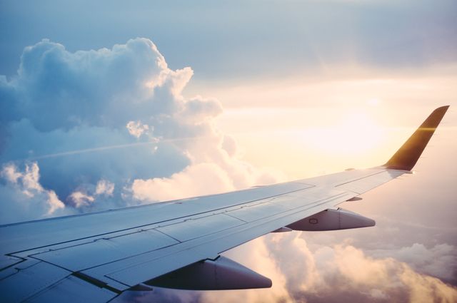 Perfect for travel blogs, aviation magazines, and tourism advertisements, this image showcases a serene view outside an airplane window featuring a wing in mid-flight with the sun setting against a backdrop of fluffy clouds. Ideal for themes related to air travel, adventure, wanderlust, and the beauty of flight.