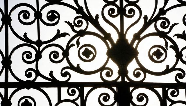 Backlit ornate wrought-iron grille creating intricate lace silhouette and symmetry