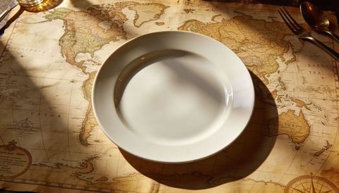 Placing white plate over vintage world map placemat casting warm sunlit shadow