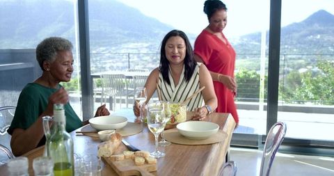 Multigenerational women sharing salad and wine on sunny terrace with mountain view