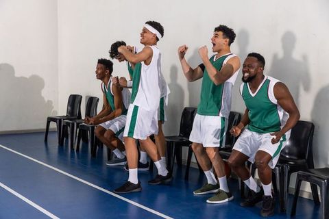 Teammates cheering energetically on basketball court sidelines