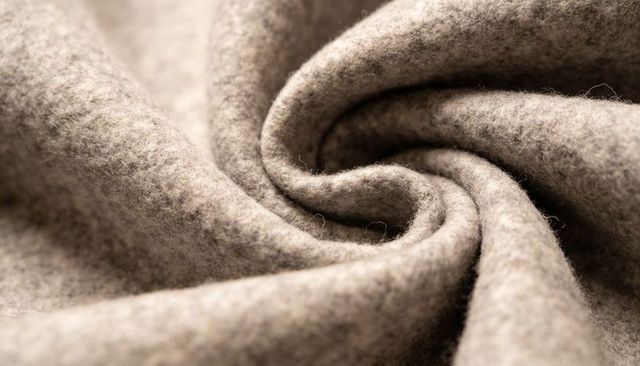 Spiral-folded beige wool fabric showing felted texture and loose fibers in macro closeup