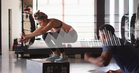 Female athlete performing plyometric box squat with trainer in gym with analytics overlay