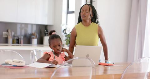 African american mother helping daughter with homework at bright modern kitchen table