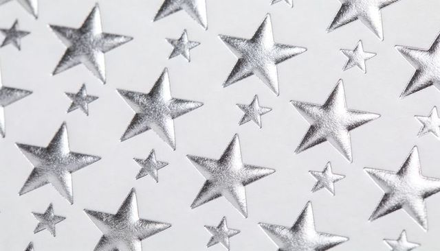 Silver embossed stars pattern on white paper showing raised foil texture reflective glossy closeup