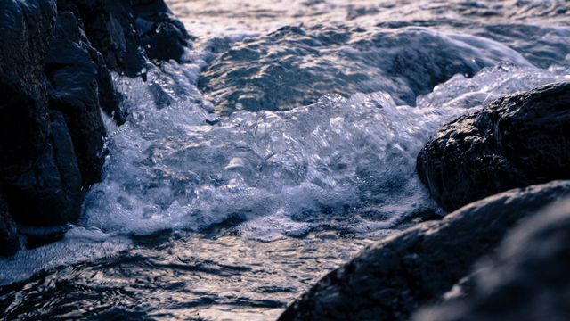 Capturing the movement of water flowing over rocks at sunset, this image conveys a sense of tranquility and natural beauty. Ideal for use in nature blogs, relaxation themes, meditation contexts, or travel advertisements aiming to showcase coastal destinations.